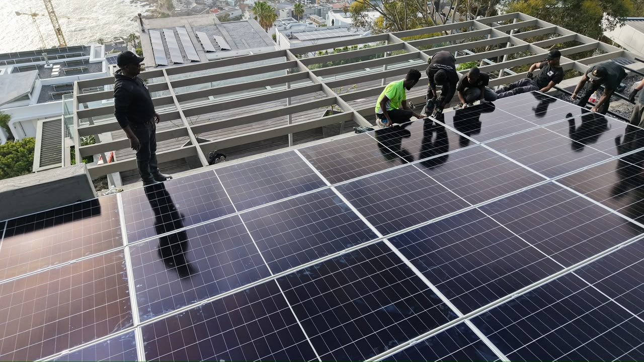 The Sun Savings install crew laying panels on a roof above the Cape Town coastline